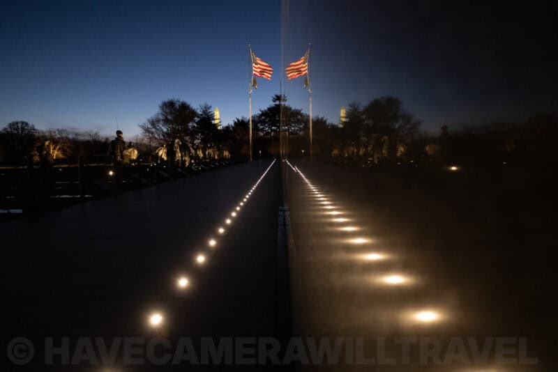 Reflective black granite path of the Vietnam Veterans Memorial lined with ground lights and flanking flags at dusk