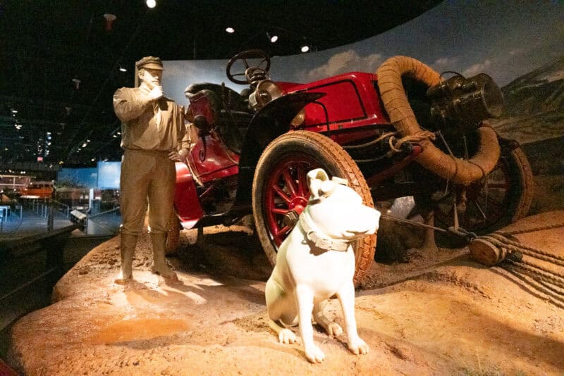 Museum exhibit of a mannequin, dog figure, and vintage red touring car, ISO 51200 sample photo