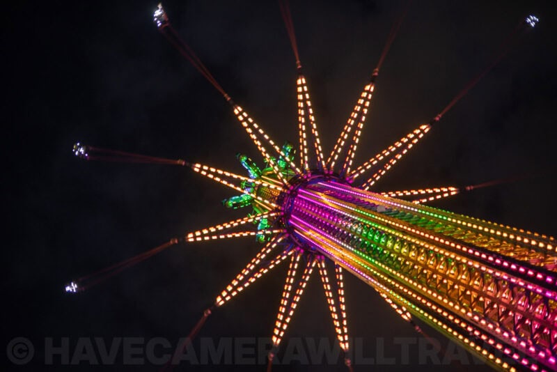 Colorful fairground swing ride lights radiating outward against a dark night sky, seen from below