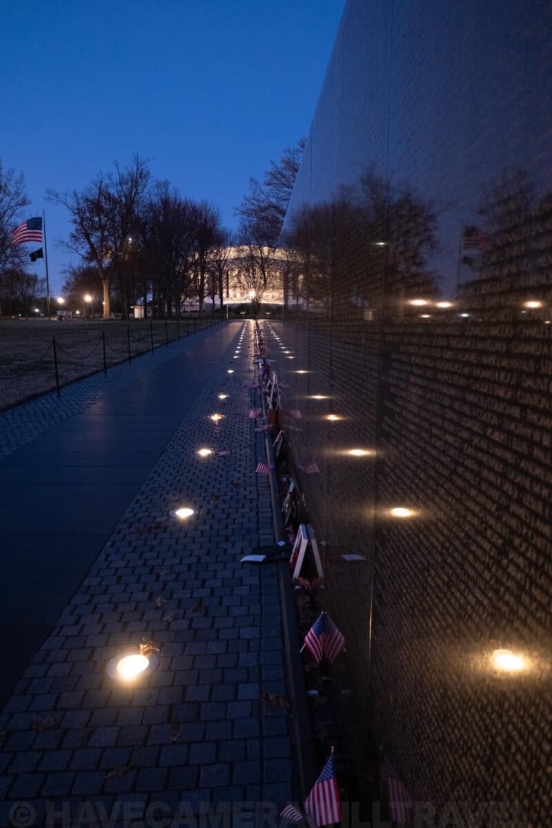 Vietnam Veterans Memorial wall reflecting the Lincoln Memorial with flags and mementos along the path