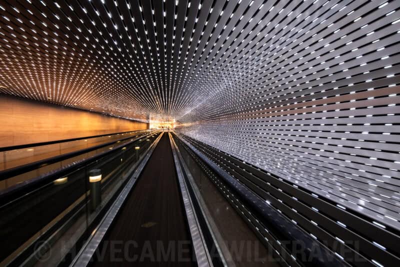 Illuminated airport moving walkway tunnel with rows of small lights converging into the distance