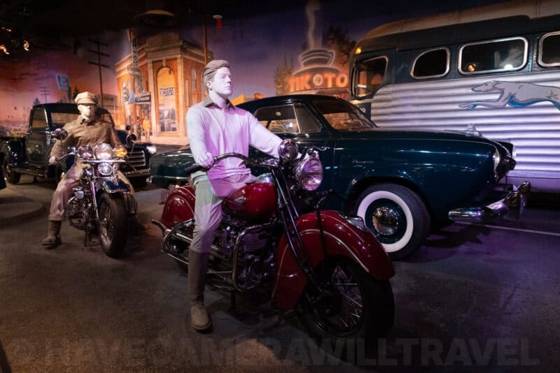 Mannequins astride antique motorcycles in front of period cars and mural backdrop, ISO 8000 sample image