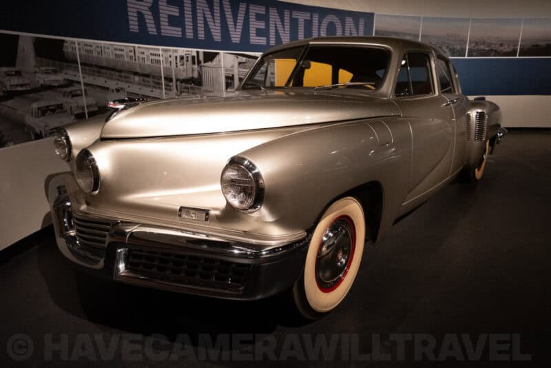 Classic Tucker sedan with chrome headlights displayed inside a history museum exhibit
