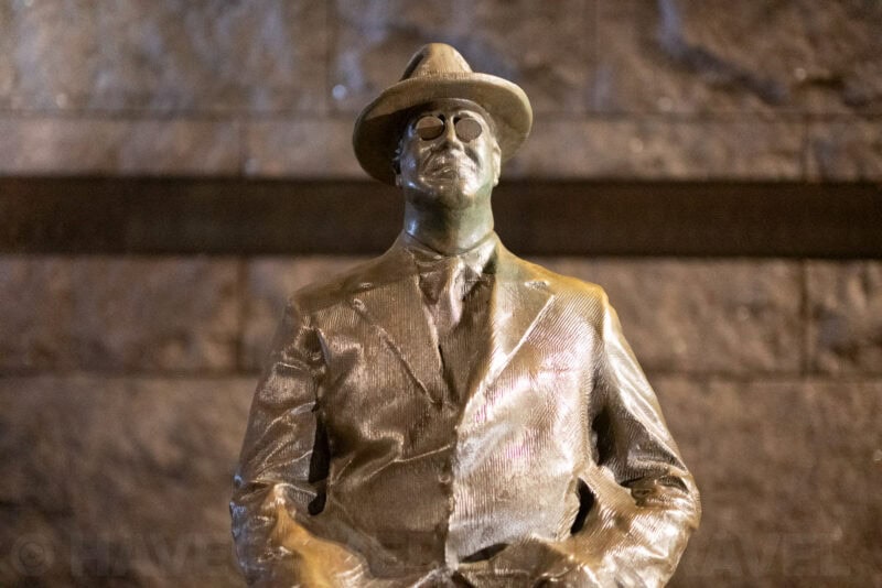 Bronze statue of a hatted, bespectacled figure at the FDR Memorial in dim light