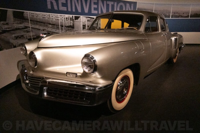 Classic silver Tucker sedan on display beneath a museum Reinvention exhibit sign