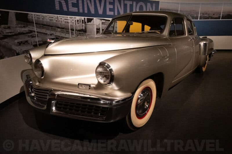 Vintage silver Tucker automobile displayed in a museum exhibit under the word Reinvention