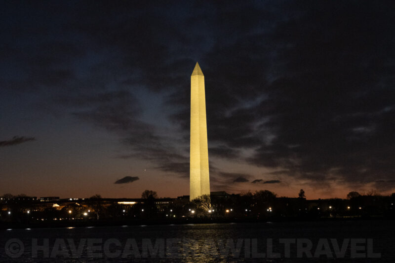 Washington Monument illuminated against a dusky cloud-streaked sky, seen across the Tidal Basin