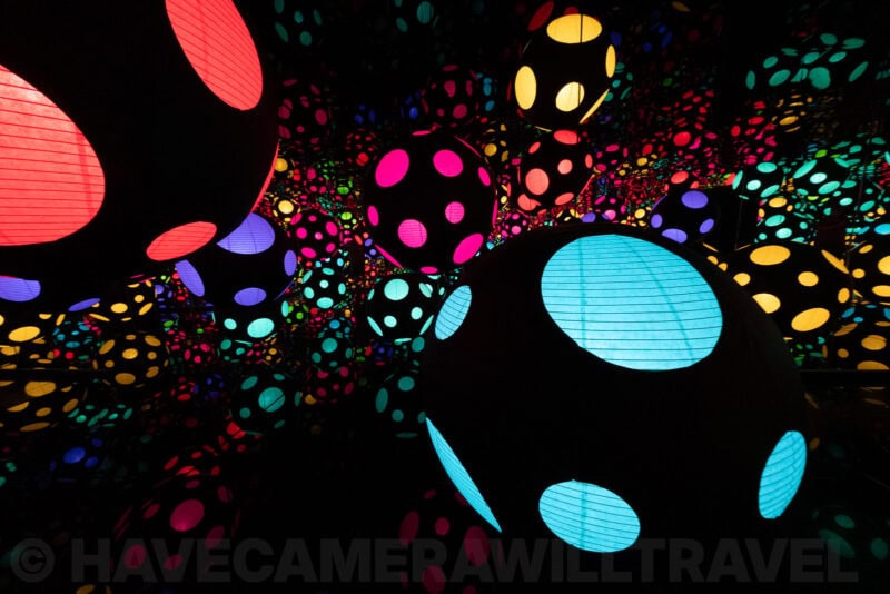 Immersive infinity room installation with glowing polka-dot spheres in red, pink and teal