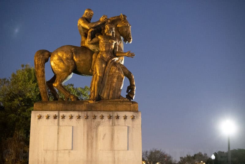 Golden equestrian statue of two figures on horseback set against a twilight sky