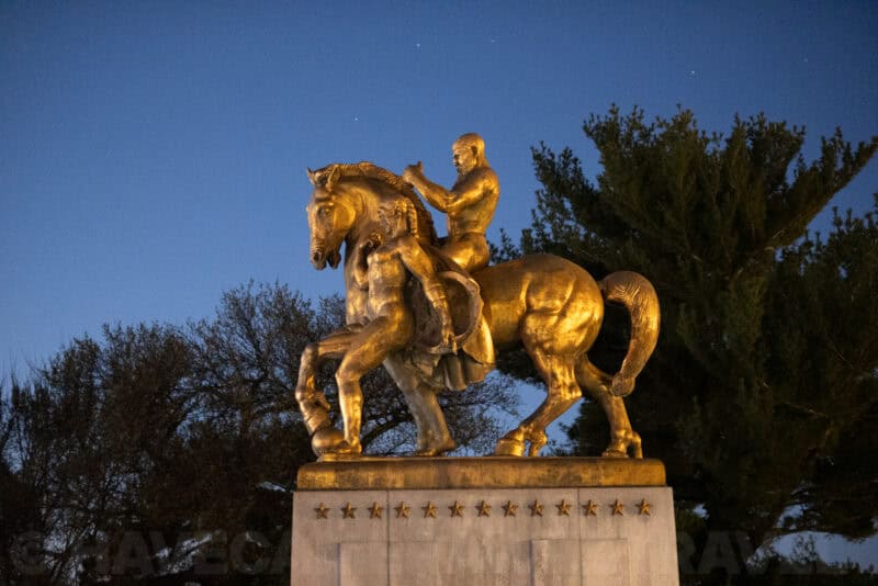 Golden equestrian statue silhouetted against a starry twilight sky with trees behind