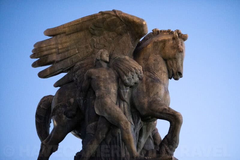 Close-up of a weathered stone statue of a winged horse and rider against a blue sky