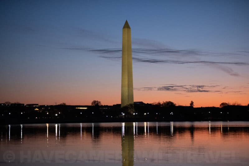 Washington Monument obelisk glowing at dusk with lights along the Tidal Basin shoreline