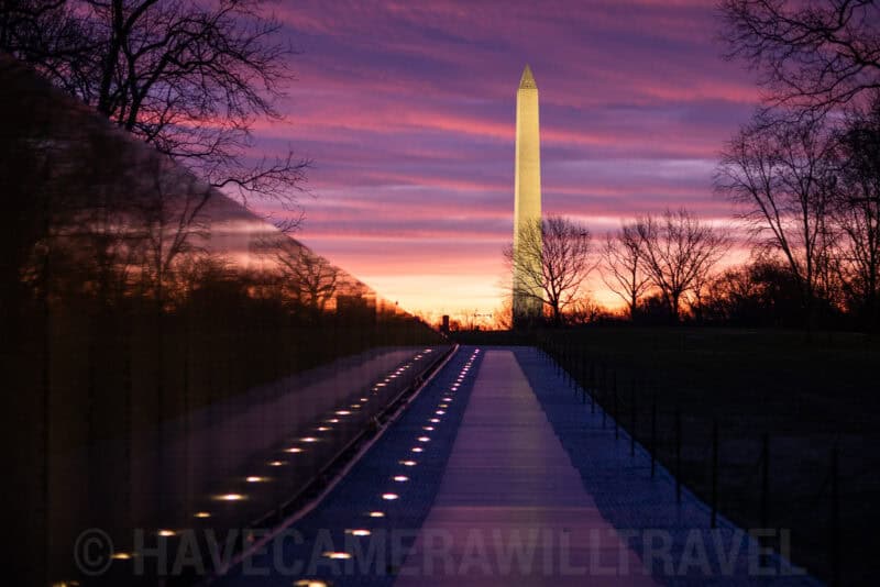 Washington Monument silhouetted against a vivid pink and orange sunrise sky above the Vietnam Veterans Memorial