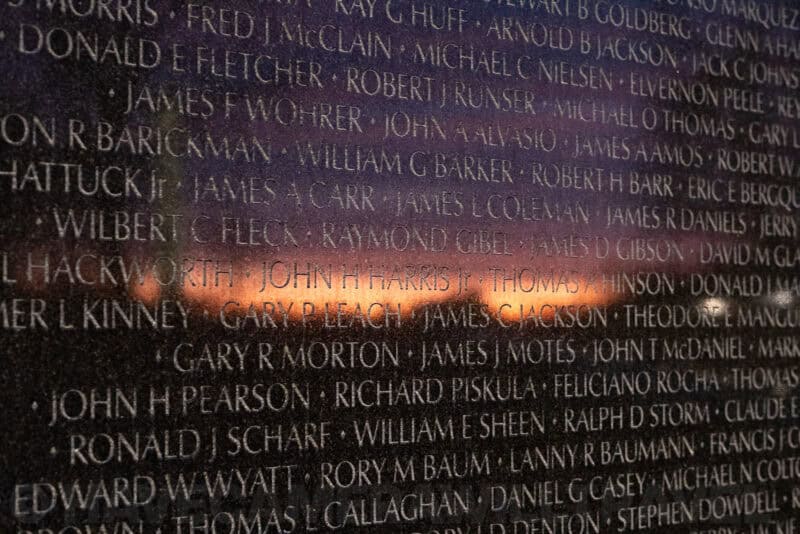 Engraved names on the Vietnam Veterans Memorial wall reflecting a colorful sunset sky