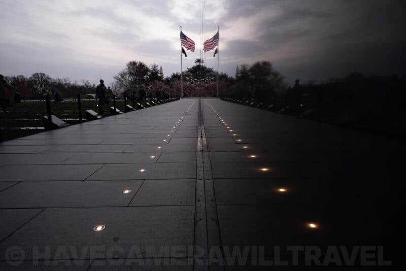 Vietnam Veterans Memorial wall reflecting flags and cherry blossoms at dusk