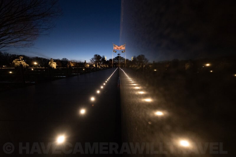 Vietnam Veterans Memorial wall reflection showing an American flag and rows of ground lights at dusk