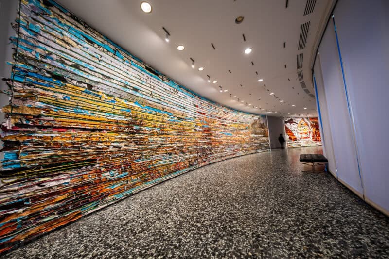Curved gallery corridor lined with a large multicolored textured art installation