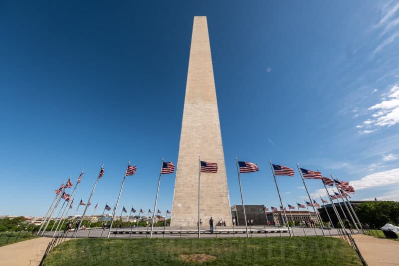 Washington Monument obelisk surrounded by a ring of American flags under blue sky