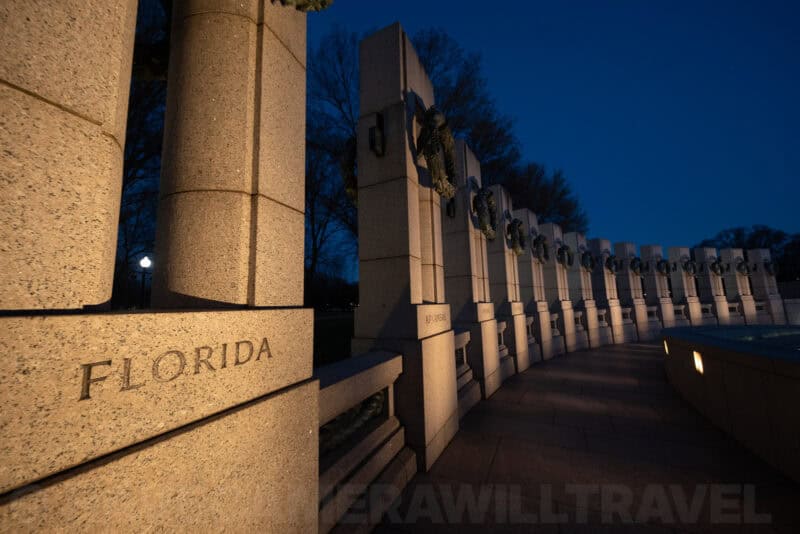 Curved row of granite pillars engraved with state names at the WWII Memorial at dusk