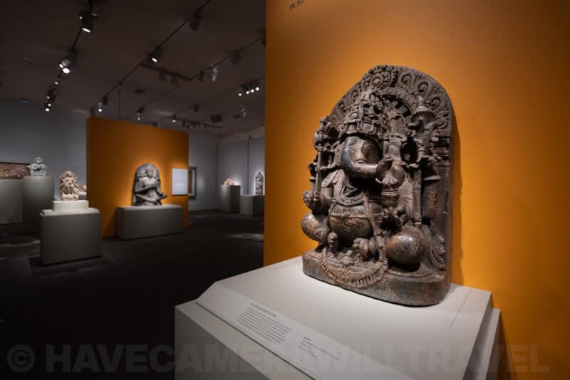 Carved stone sculpture of Ganesha displayed in a museum gallery with orange-lit walls