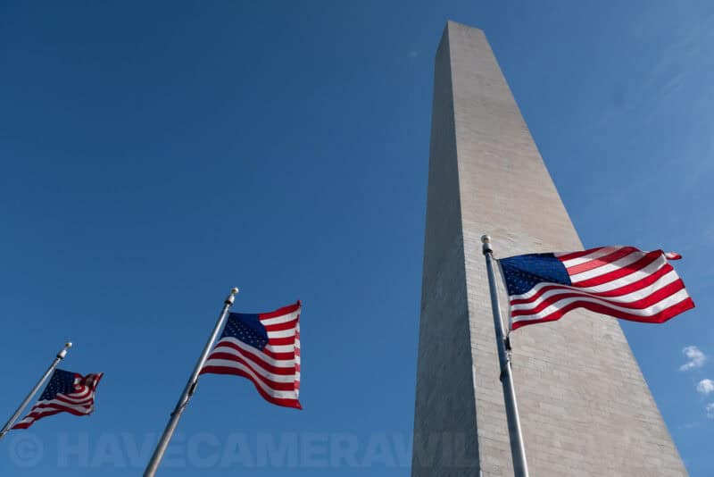 Washington Monument obelisk rising above waving American flags under a clear blue sky