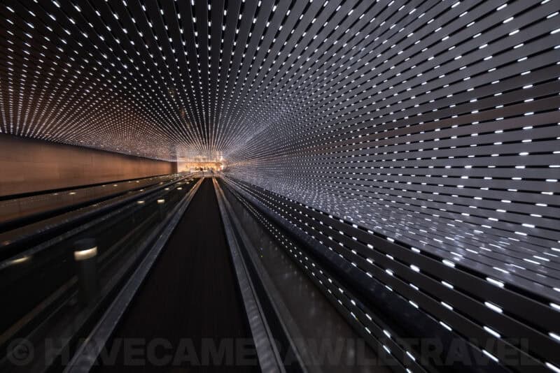 Ultra-wide view down an illuminated moving walkway tunnel with streaking light patterns