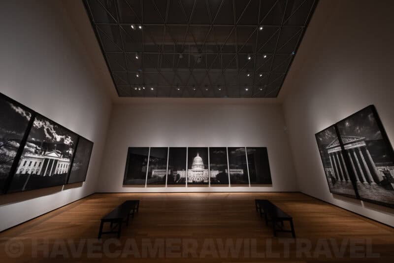 Wide gallery view of large charcoal drawings of the White House and U.S. Capitol on museum walls
