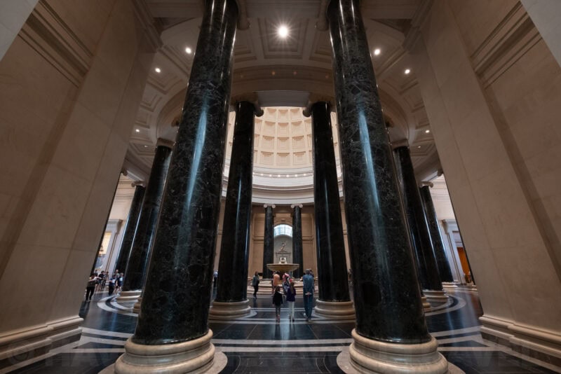 Dark marble columns framing a fountain and museum visitors under a coffered dome