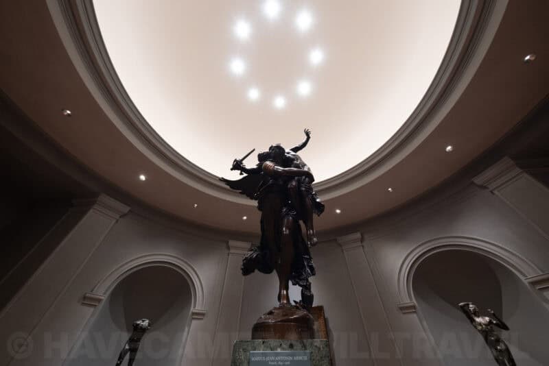 Bronze sculpture of dueling figures beneath a domed skylight with ring of ceiling lights