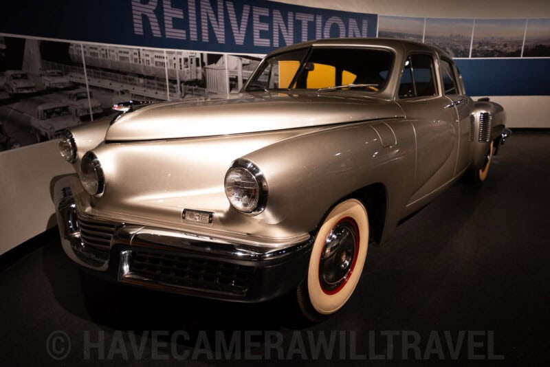 Vintage Tucker automobile on display under a museum exhibit banner reading Reinvention
