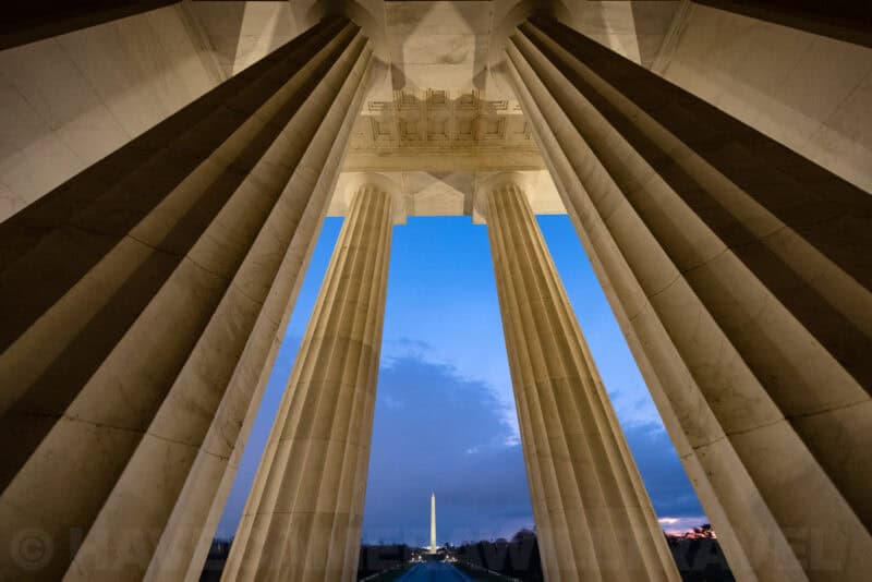 Lincoln Memorial columns framing a distant view of the Washington Monument at dusk