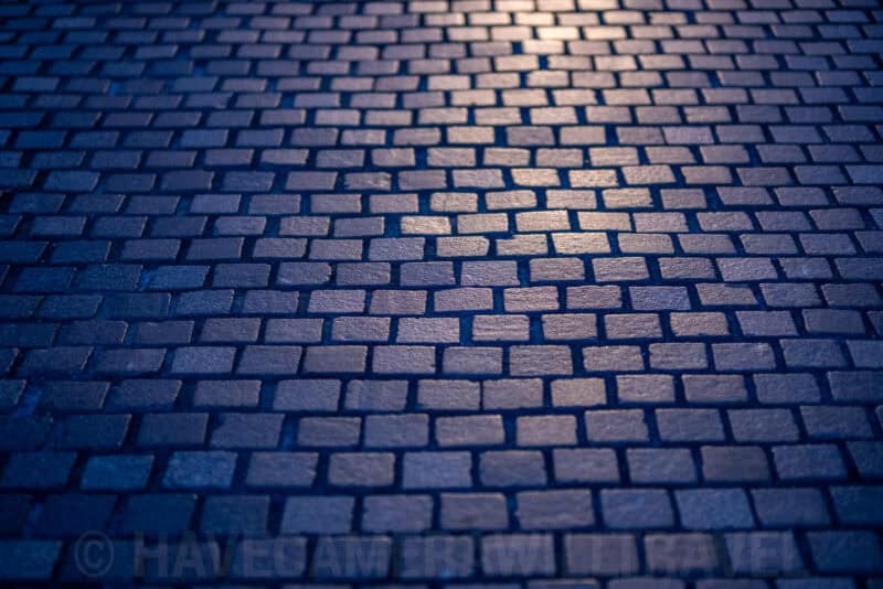 Close-up of wet cobblestone pavement reflecting warm light at night