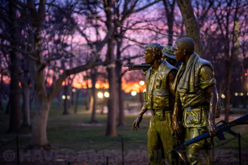 Three Soldiers bronze statue at the Vietnam Veterans Memorial against a colorful sunset sky