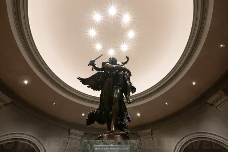 Bronze angel statue beneath a domed ceiling with star-shaped spotlight flares