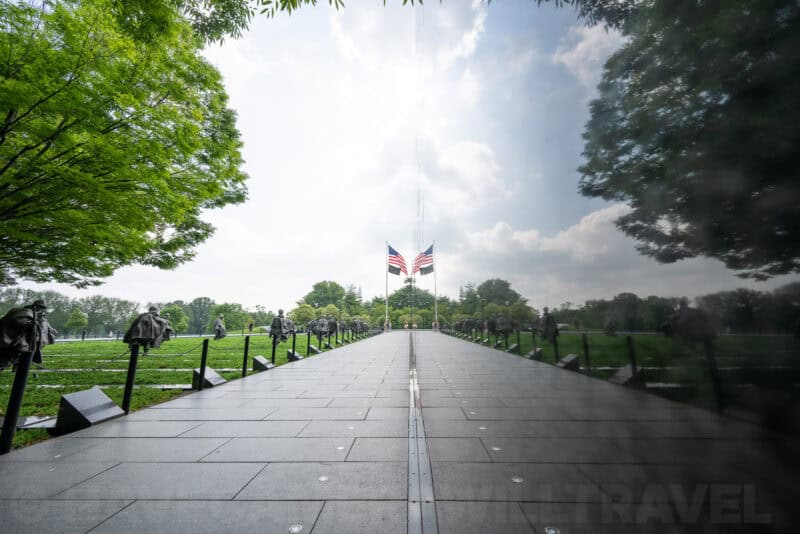 Reflective black granite wall of the Korean War Veterans Memorial mirroring trees, sky, and flags