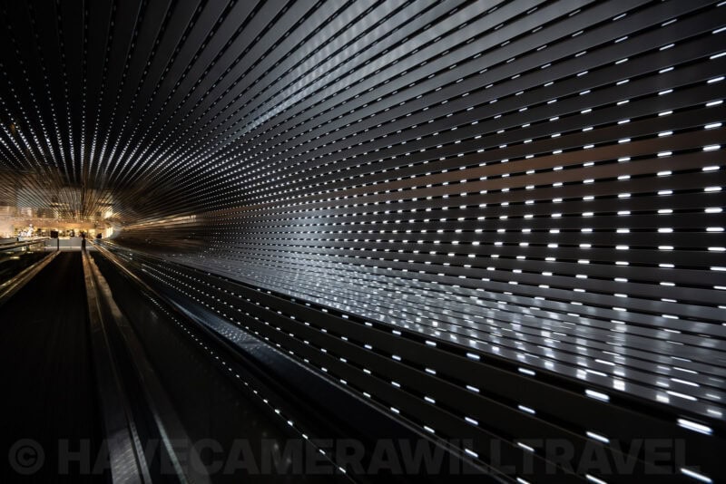 Wide-angle view of a ribbed metallic tunnel installation with rows of glowing white light slits