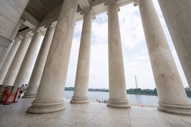 Row of marble columns at the Jefferson Memorial framing a view of the Washington Monument across the water