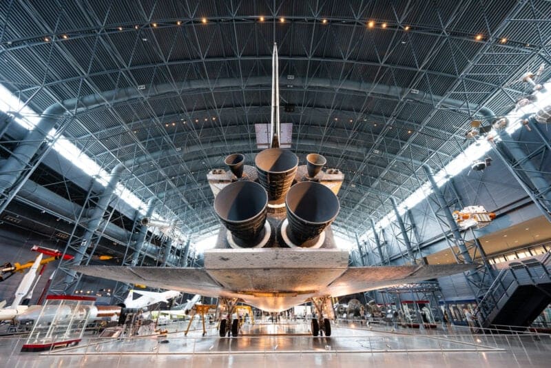 Rear view of a space shuttle's engine nozzles under the vaulted roof of the Udvar-Hazy Center hangar