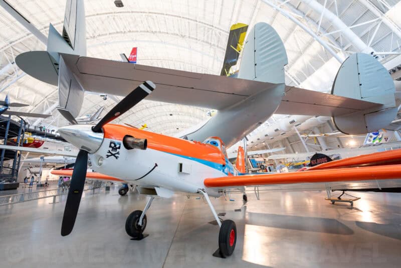 Vintage orange and white propeller airplane displayed beneath a hangar's arched ceiling