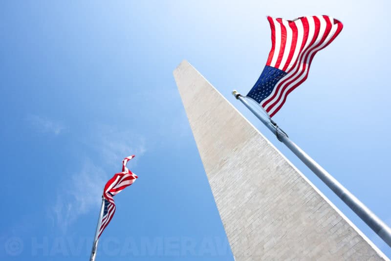 American flags flying beside the Washington Monument's obelisk against a bright blue sky