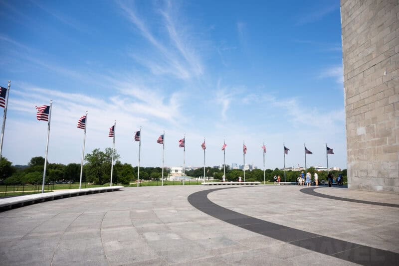 Row of American flags lining a curved plaza with the Lincoln Memorial visible in the distance