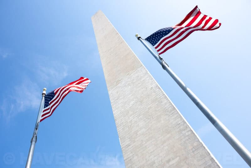 Washington Monument obelisk seen from below flanked by two waving American flags