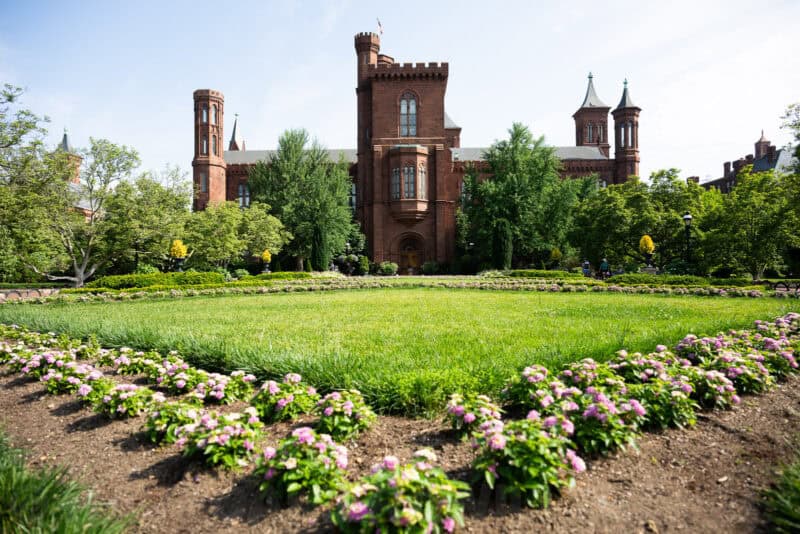 Smithsonian Castle in Washington DC, its red sandstone turrets framed by lawn and pink flower beds