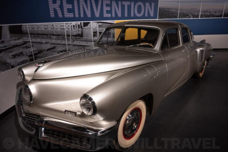 Vintage silver Tucker sedan on display in front of a museum wall reading 'Reinvention'