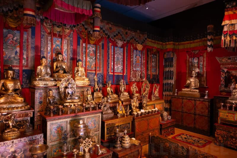 Tibetan Buddhist shrine room display with gilded Buddha statues and red patterned wall hangings