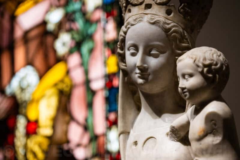 Marble Madonna and Child statue in close-up beside a colorful stained-glass window