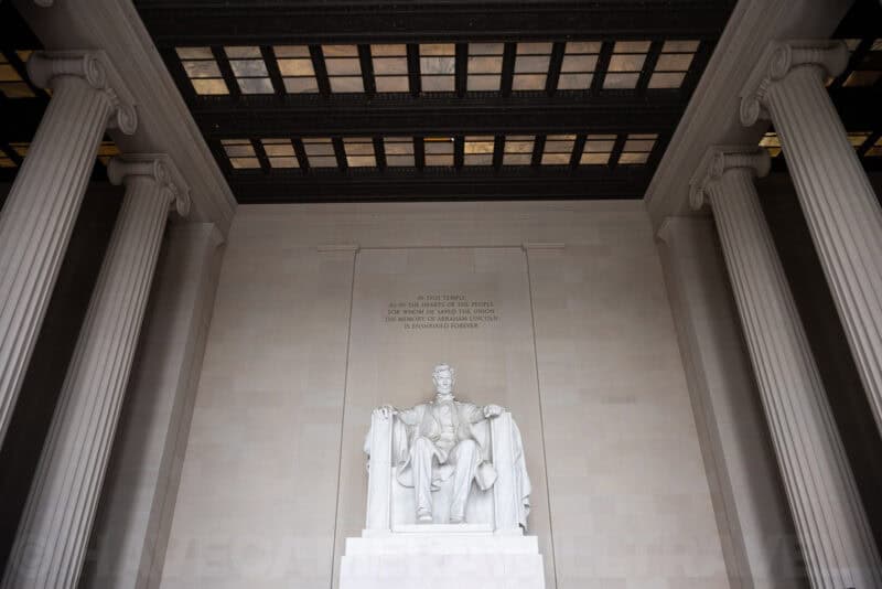 Lincoln Memorial statue framed by tall marble columns and coffered ceiling, viewed from below