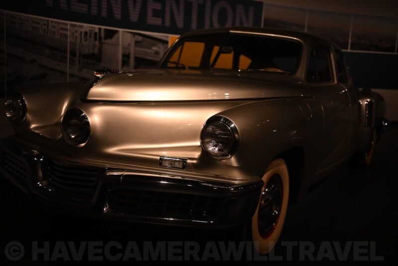 Silver Tucker automobile front end with round headlights displayed under a dim spotlight in a museum