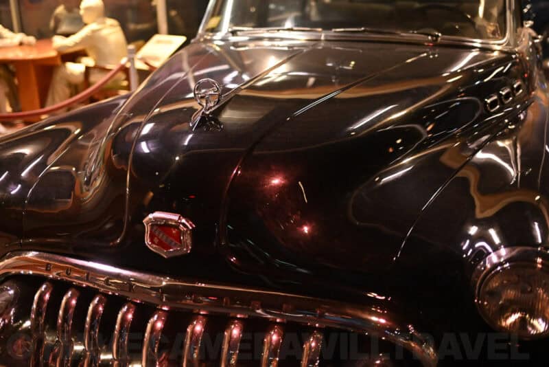 Close-up of a glossy black classic Buick hood ornament and grille under low museum lighting
