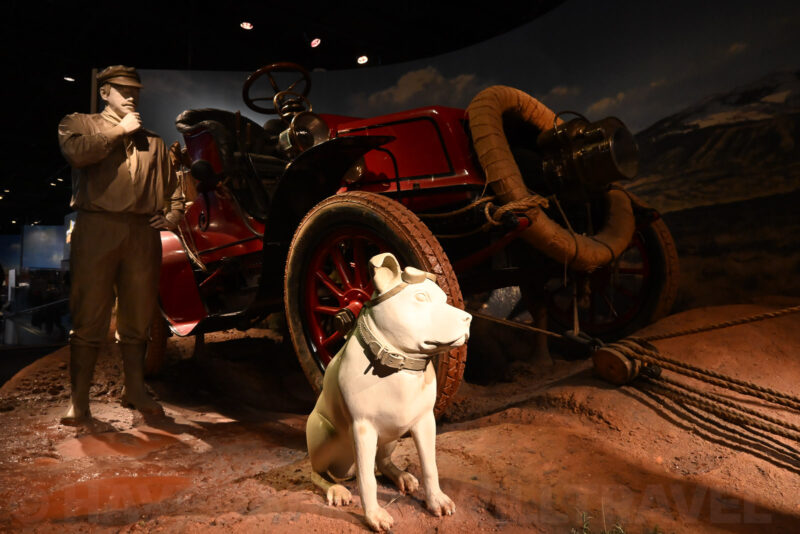 Museum diorama of a vintage red car with a man and dog statue beside it, likely a Smithsonian exhibit